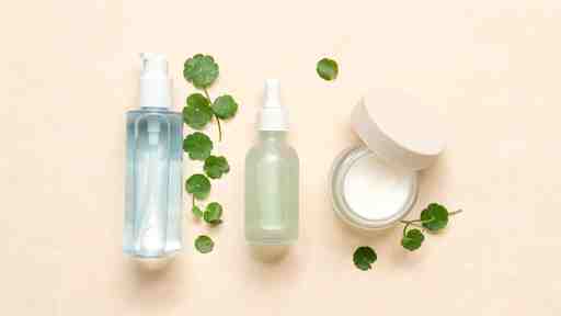 Flat lay of centella (cica) Korean skincare products with green botanical leaves on a soft neutral background