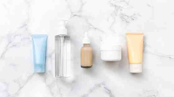Flat lay of affordable Korean skincare products — gel cleanser, toner, snail mucin essence, ceramide cream, and sunscreen — on a white marble surface