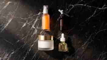 Flat lay of anti-aging Korean skincare — vitamin C serum, retinol, peptide cream, and facial oil — on dark marble