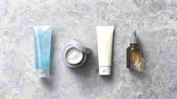Flat lay of men's Korean skincare essentials — cleanser, lightweight moisturizer, sunscreen, serum — on a concrete grey surface
